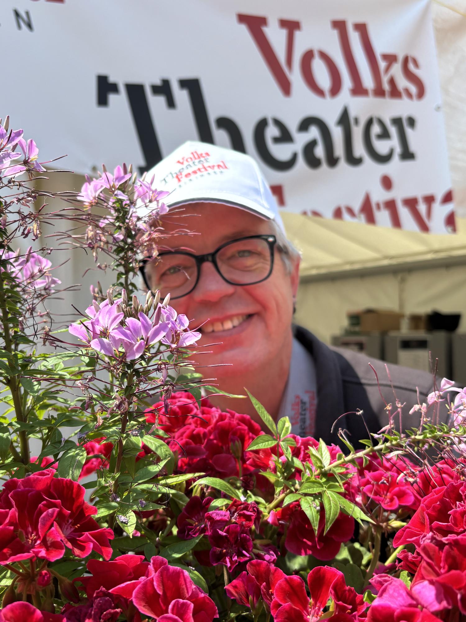 A member of the organising committee behind flowers in front of the festival tent 2026
